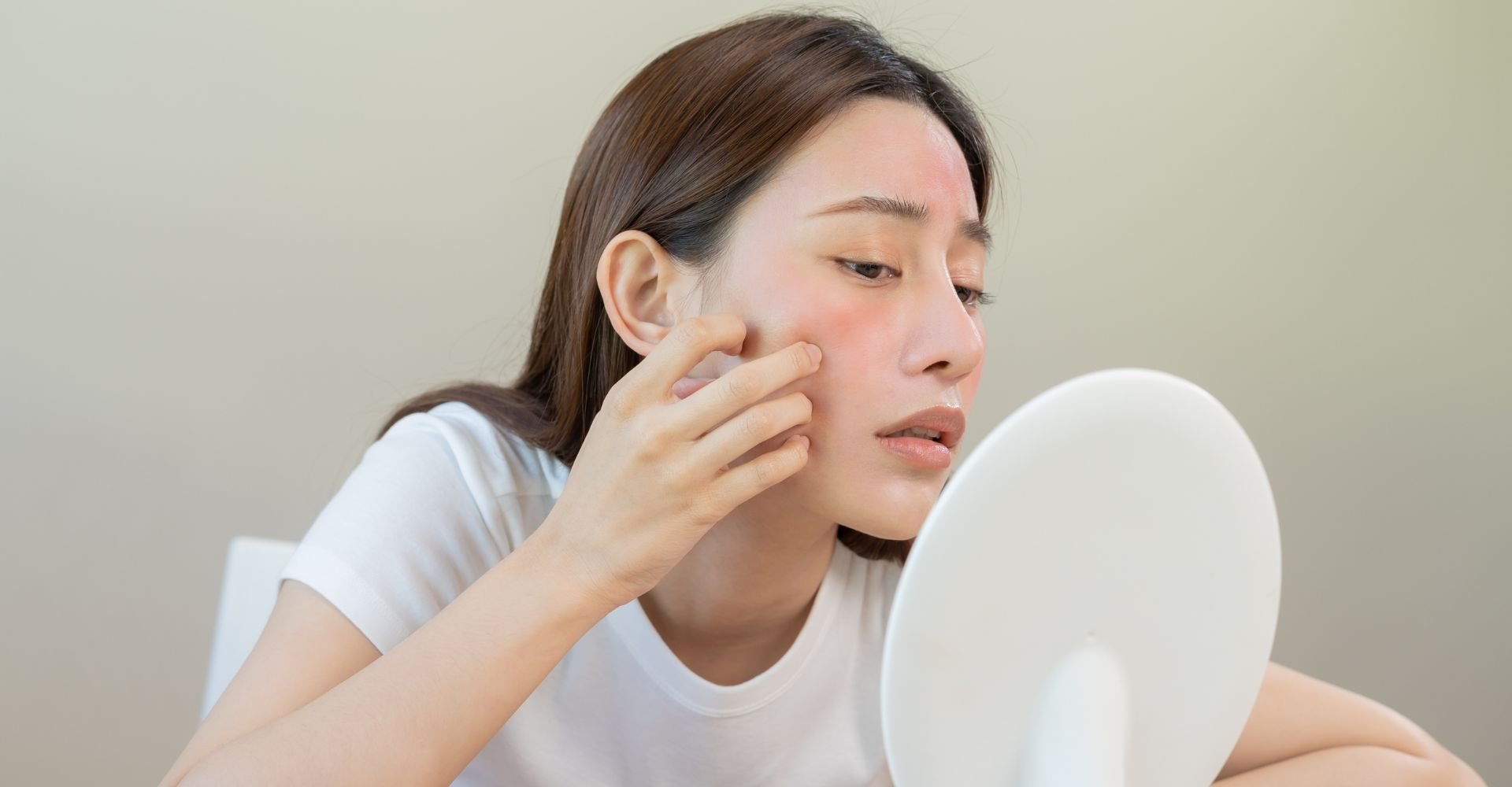  Mulher olhando no espelho e vendo pele com manchas vermelhas no rosto.