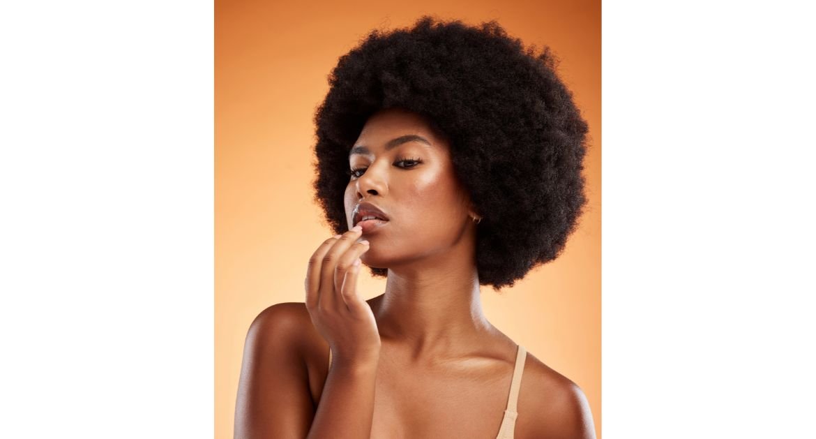 Mulher tocando seus lábios que estão com lip oil enquanto usa maquiagem simples em seu rosto.