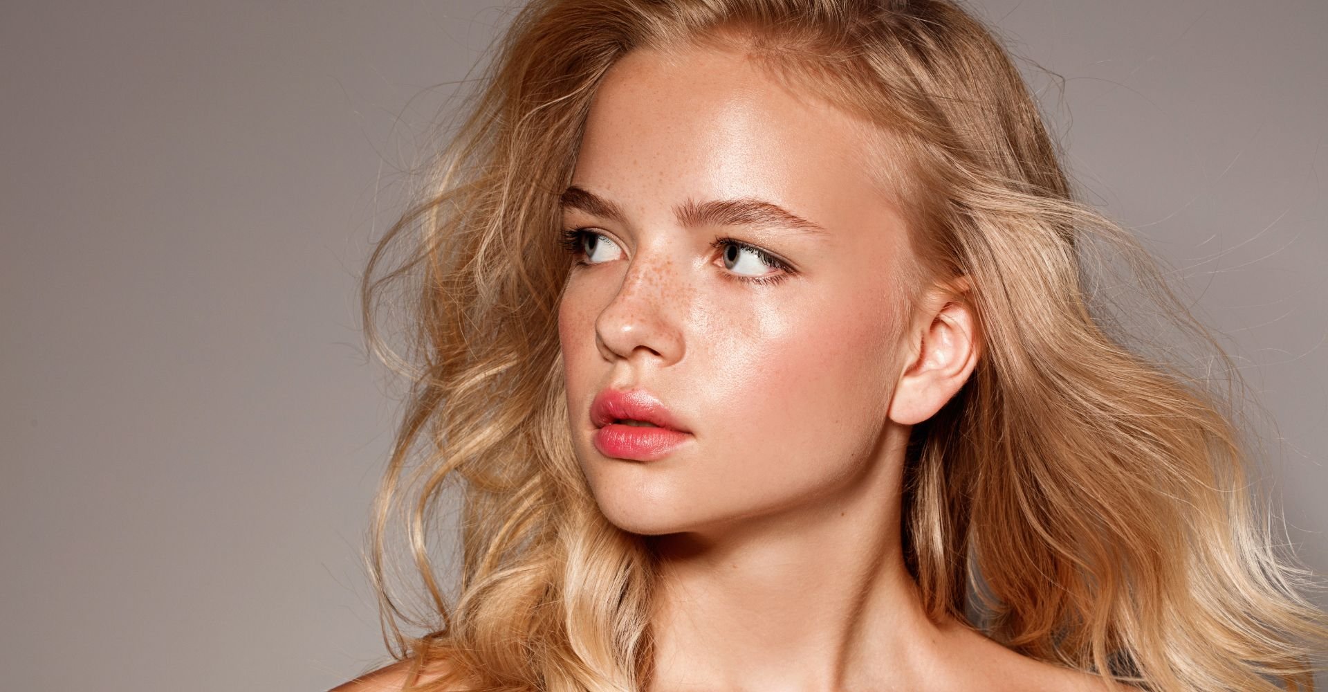 Menina loira com maquiagem simples no seu rosto com lábios pêssego e blush rosa nas bochechas.