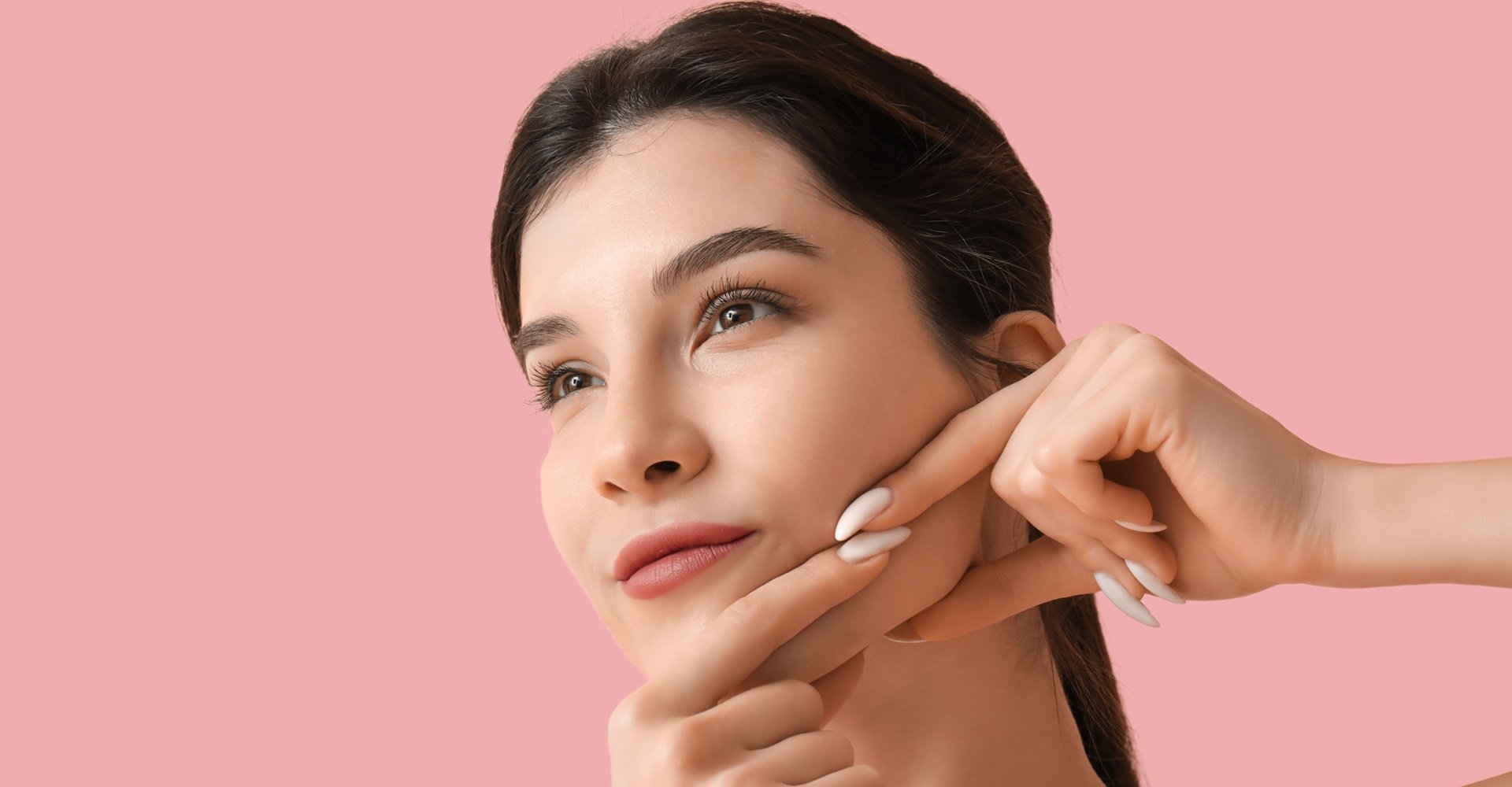 Mulher fazendo massagem facial no rosto em fundo rosa.