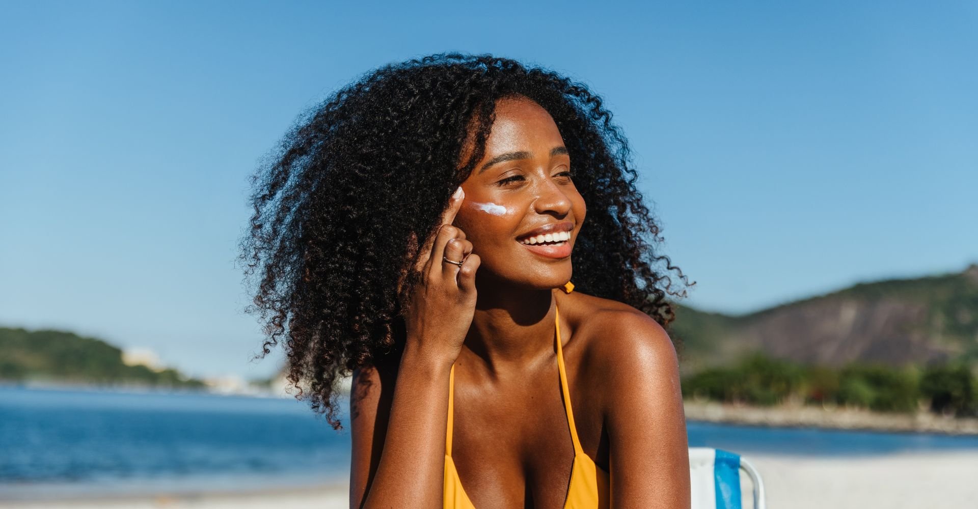 Jovem mulher negra aplicando um protetor solar fator 70 no rosto para proteger sua pele