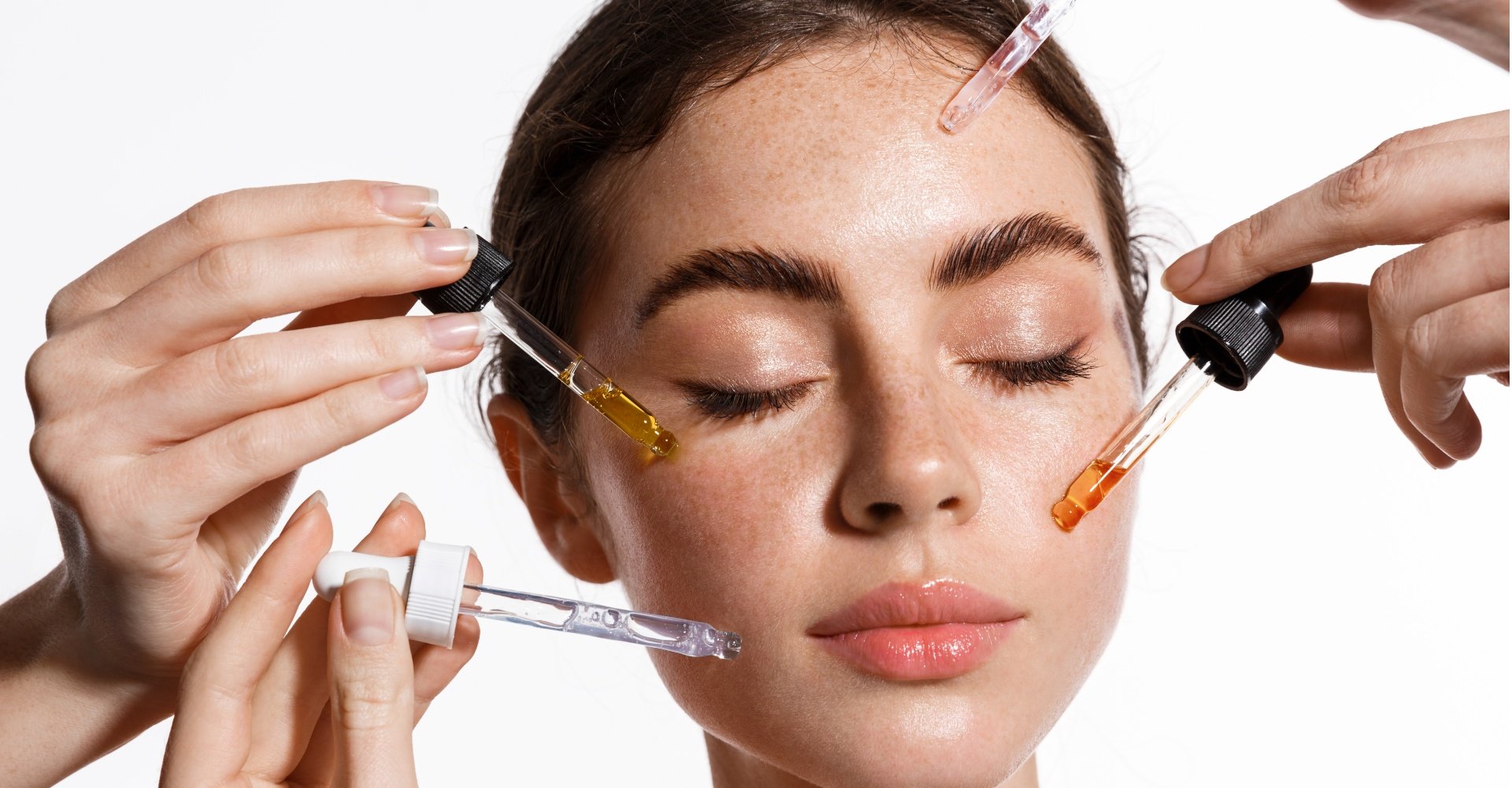 Mãos com conta-gotas de soro com sérum facial perto do rosto da mulher.