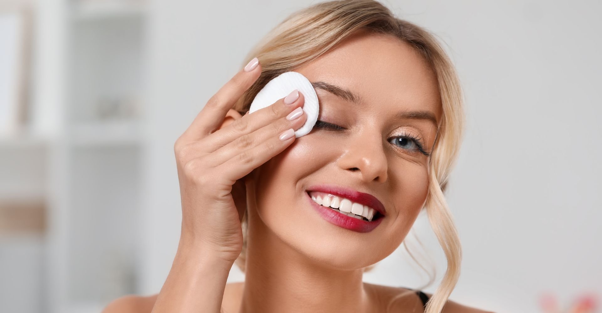 Jovem caucasiana sorridente aplica tônico facial em seu rosto com disco de algodão