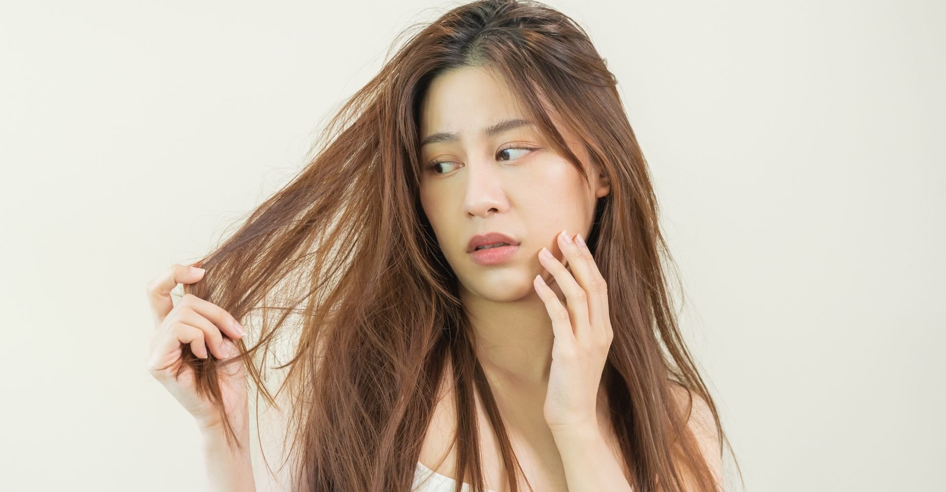 Mulher olhando o cabelo com a mão esquerda na bochecha em um fundo branco.