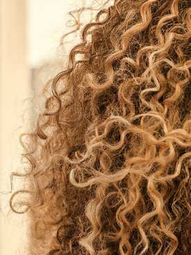 Mulher com cabelos loiros, cacheados e volumosos contra o sol.
