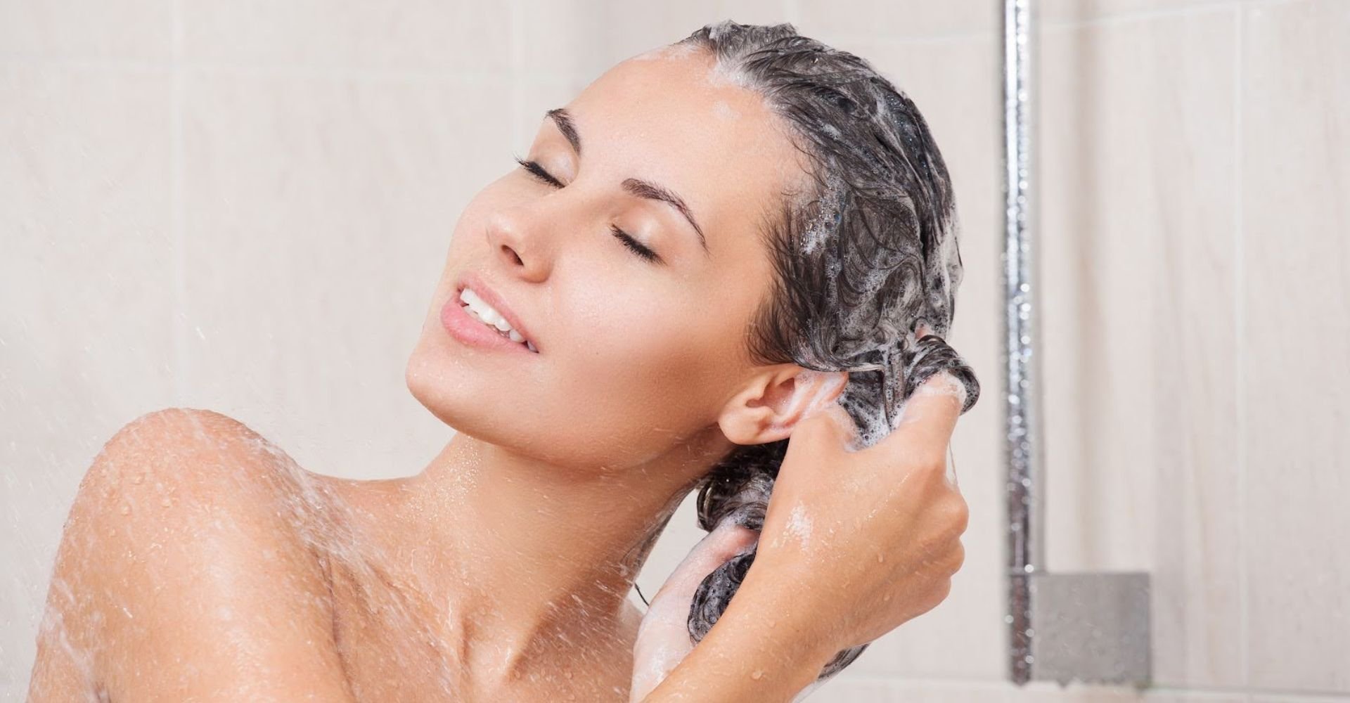 Mulher de olhos fechados, tomando banho e lavando o cabelo em sua rotina de cuidados com o cabelo.