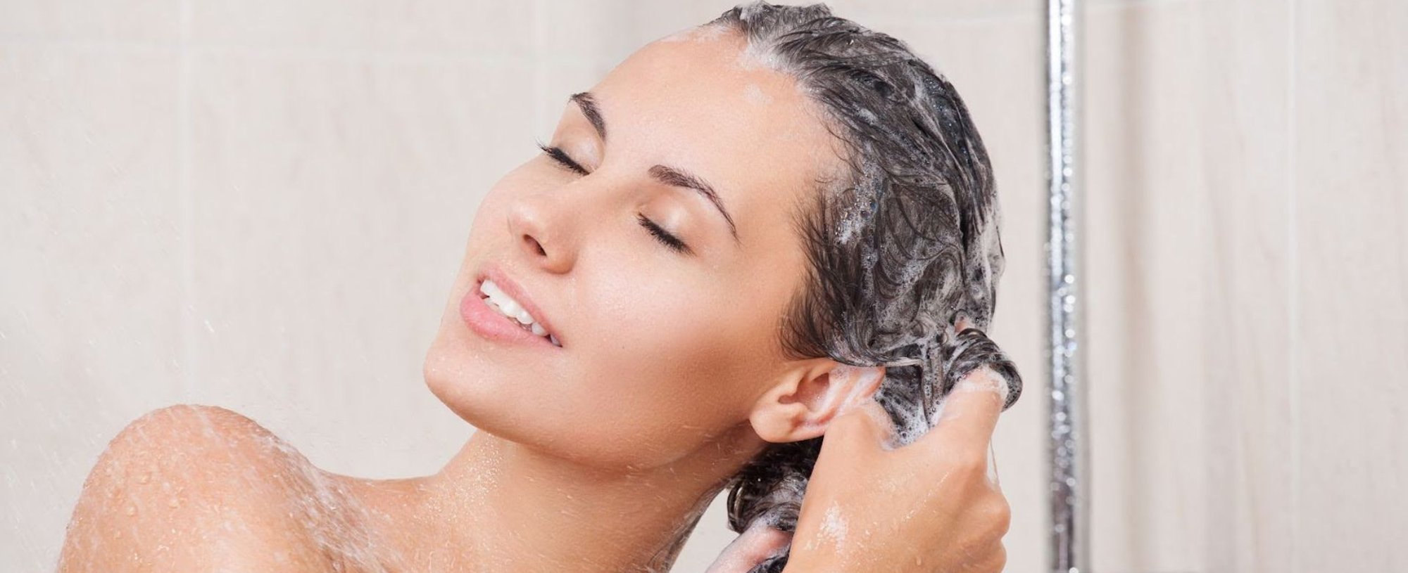 Mulher de olhos fechados, tomando banho e lavando o cabelo em sua rotina de cuidados com o cabelo.