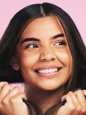 Mulher sorridente segurando seu cabelo com as mãos em fundo rosa.
