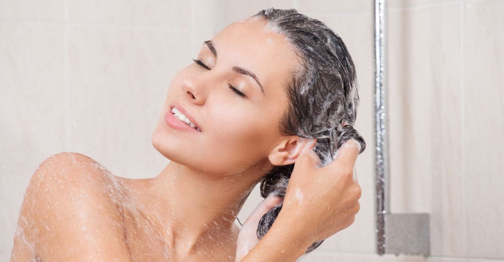 Mulher de olhos fechados, tomando banho e lavando os cabelos.