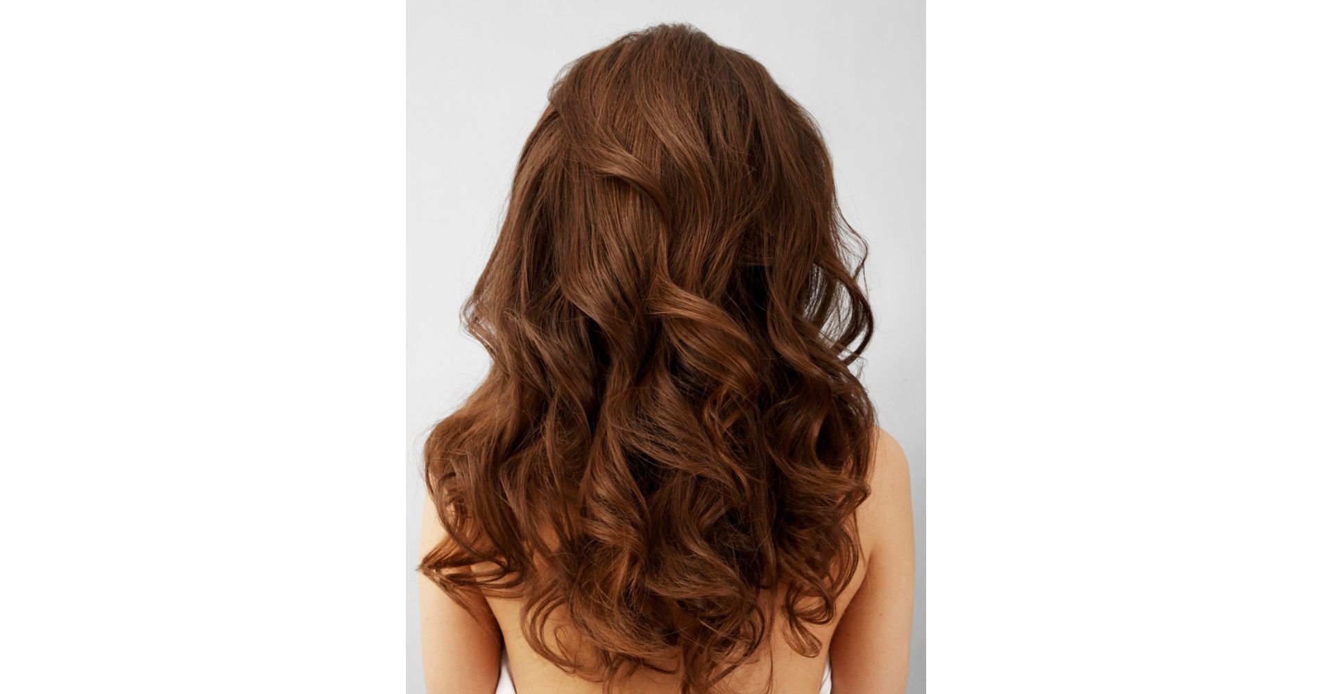 Cabelo longo e ondulado na cor caramelo, com reflexos quentes e dourados, visto por trás sobre fundo cinza claro.