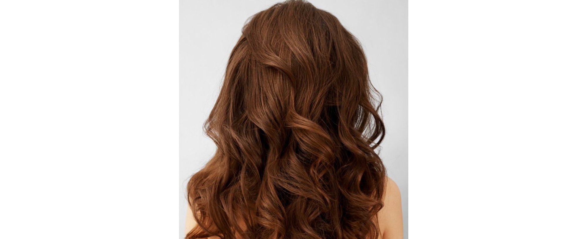 Cabelo longo e ondulado na cor caramelo, com reflexos quentes e dourados, visto por trás sobre fundo cinza claro.
