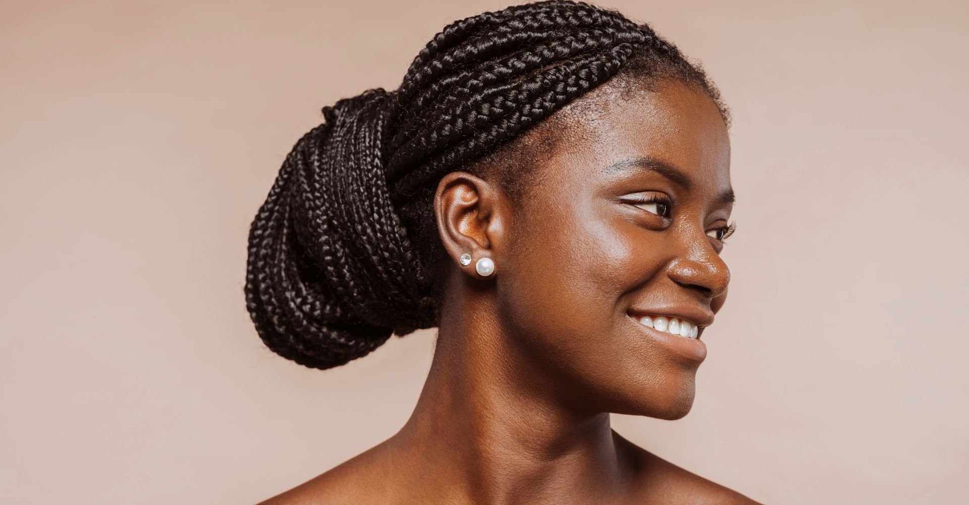 Jovem negra sorrindo com um penteado de formatura de cabelo longo em fundo neutro.