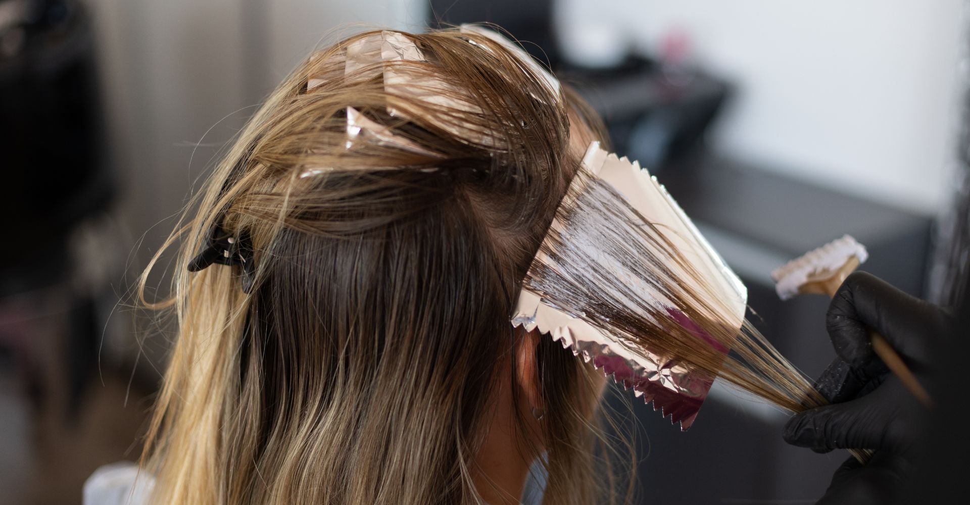 Mulher no cabeleireiro com o cabelo separado sendo pintado por um(a) profissional.