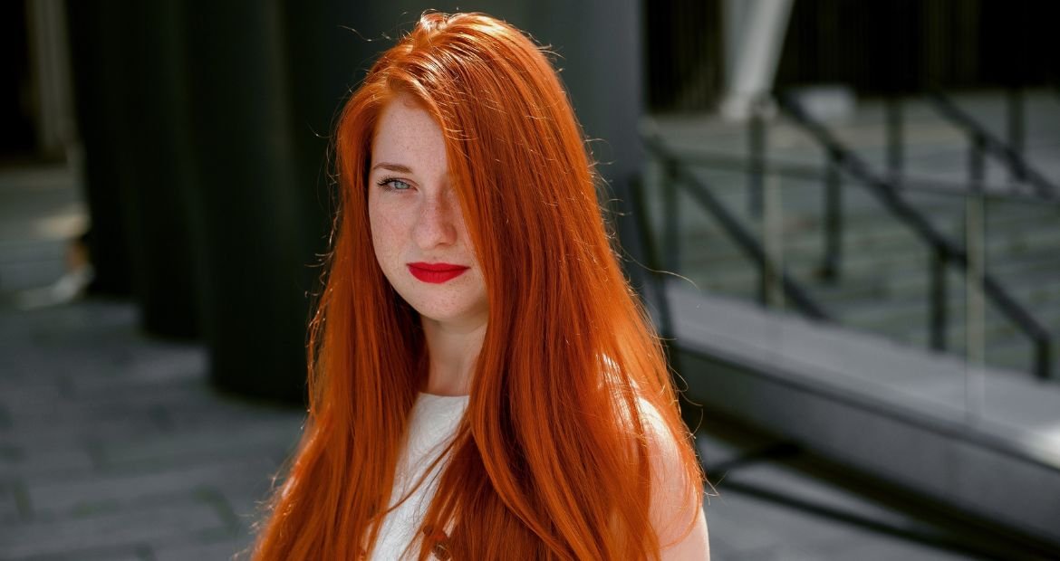Menina com cabelo ruivo alaranjado usando batom vermelho nos lábios.