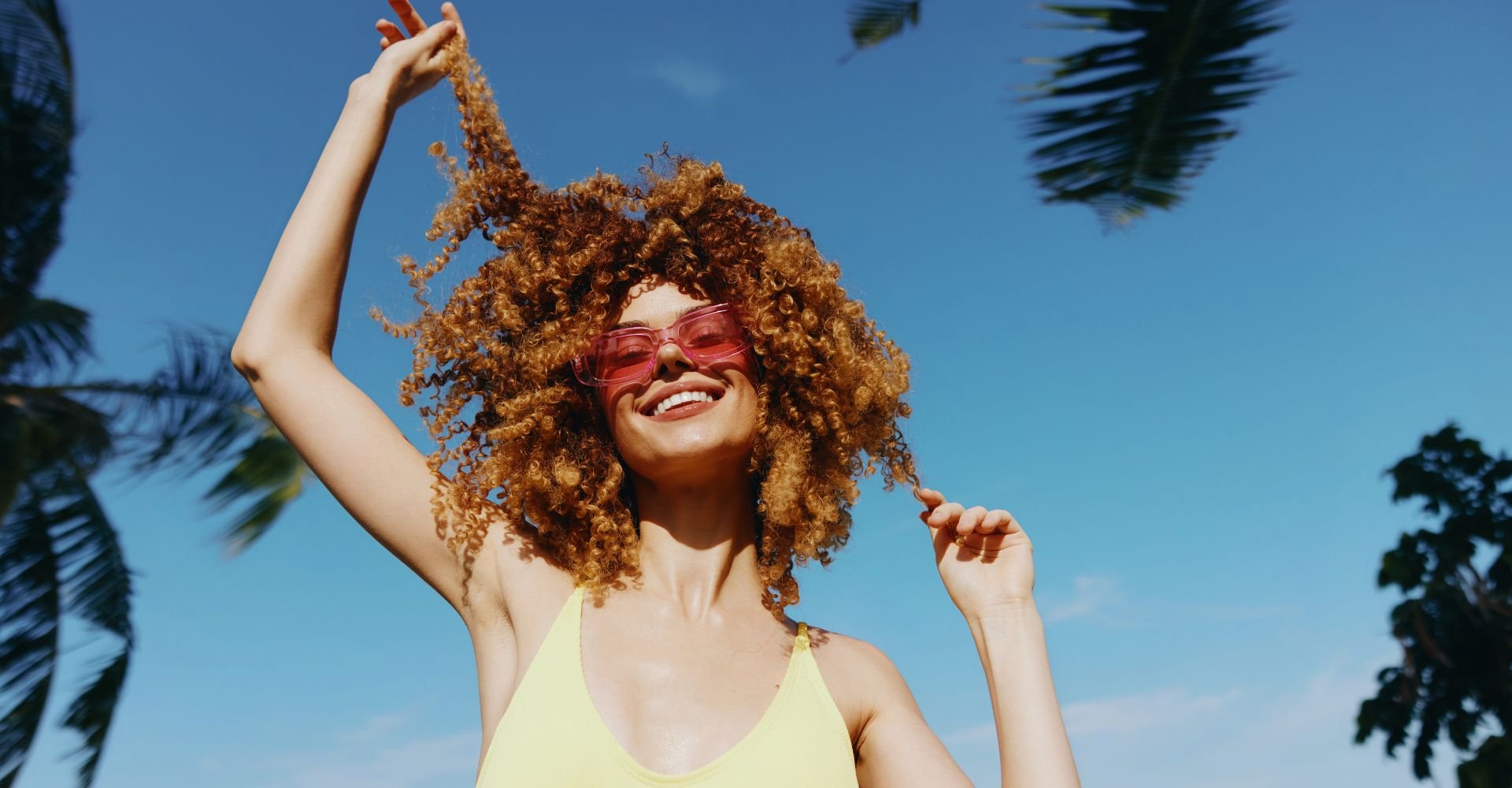 Mulher sorridente com o cabelo cacheado e com brilho ao recuperar o cabelo opaco.