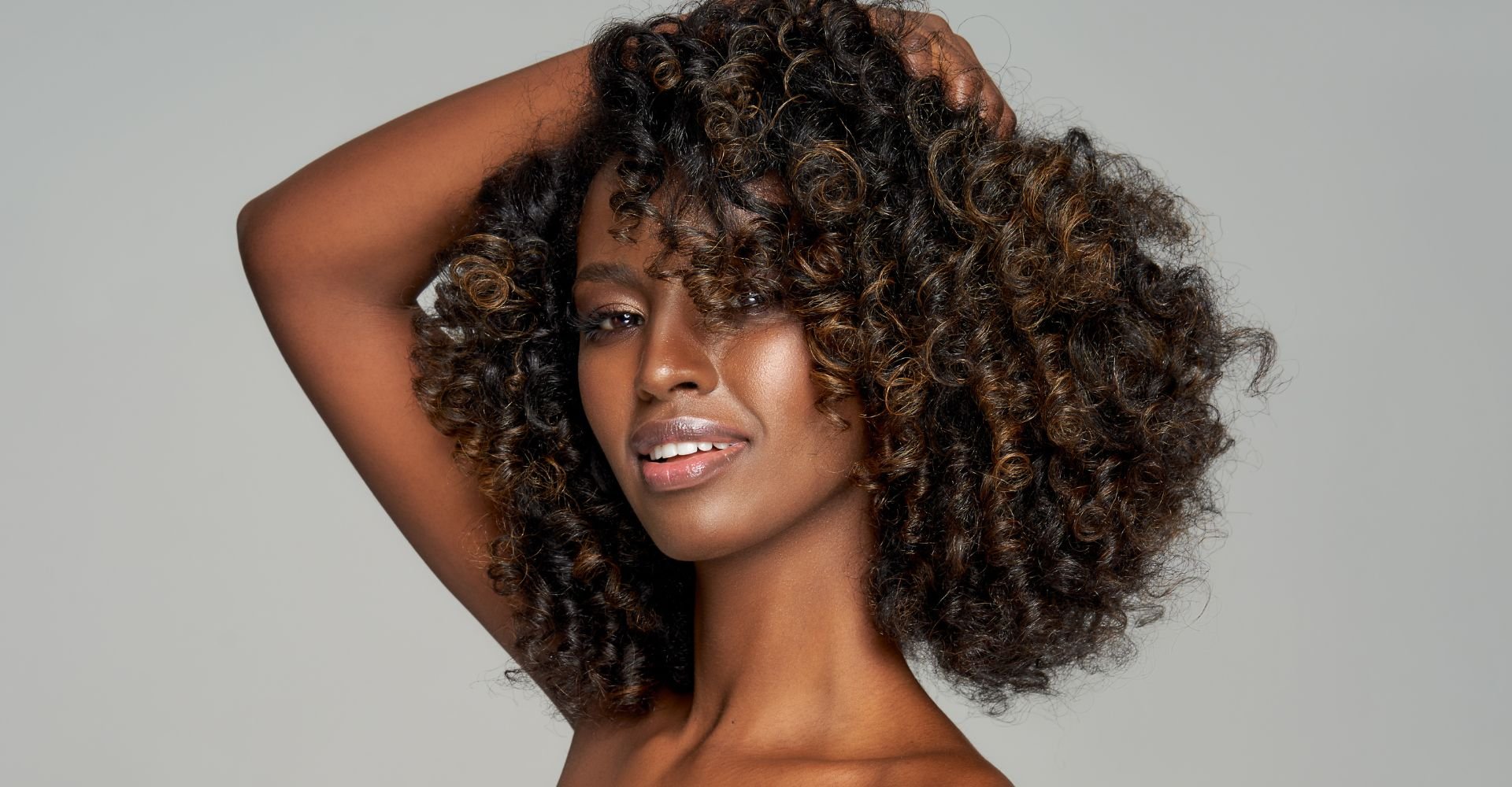 Mulher negra sorridente após fazer banho de brilho no cabelo e renovar a cor.