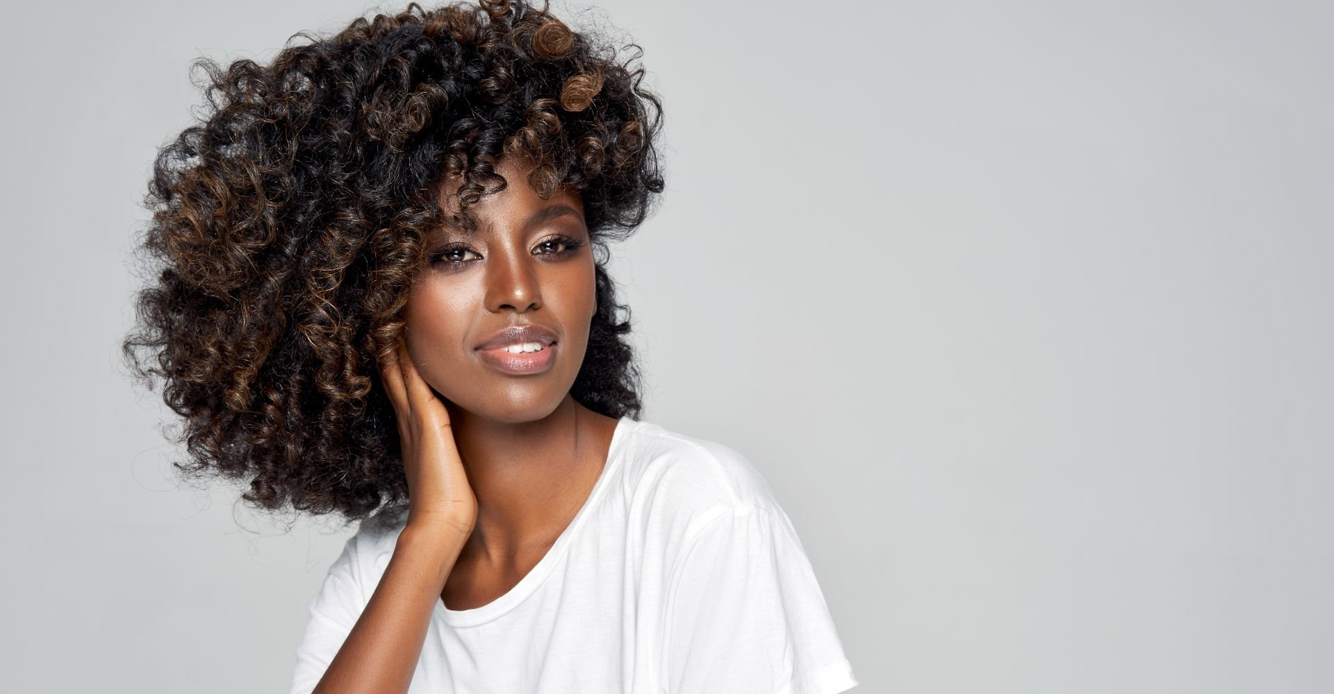 Mulher negra sorridente após fazer banho de brilho no cabelo e renovar a cor.