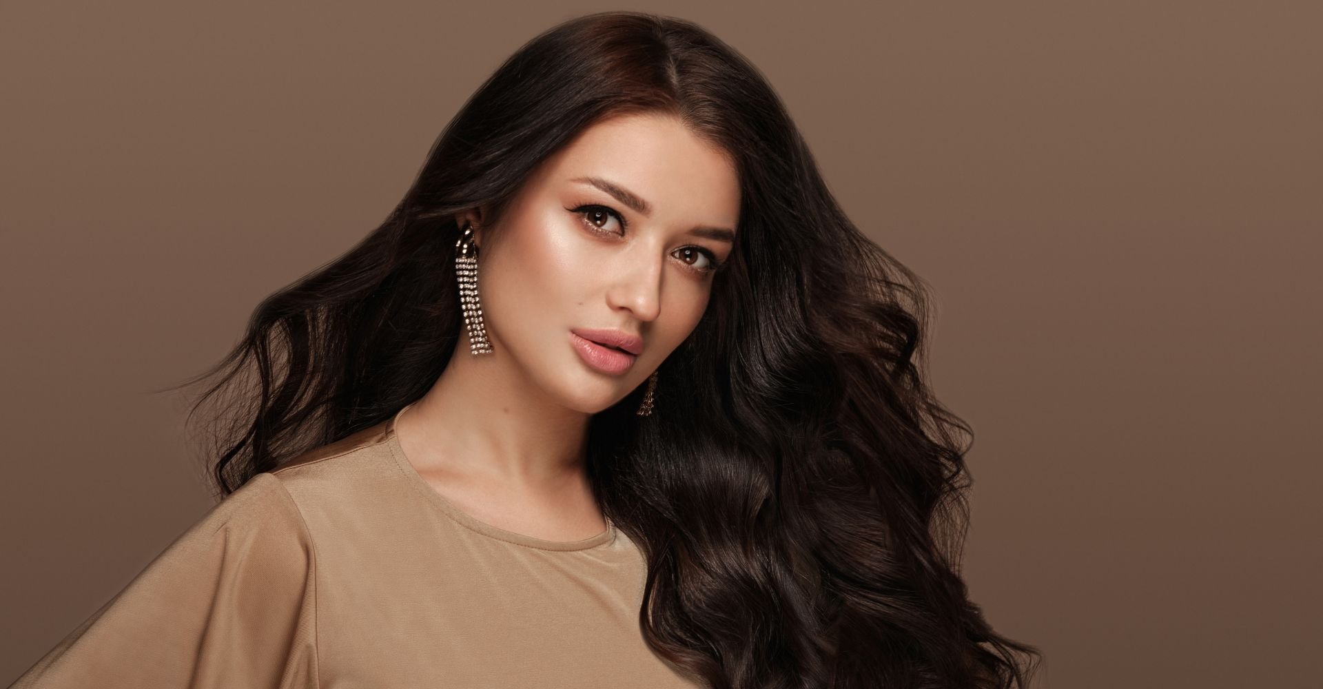 Mulher com cabelo preto olhando para a câmera em fundo marrom.