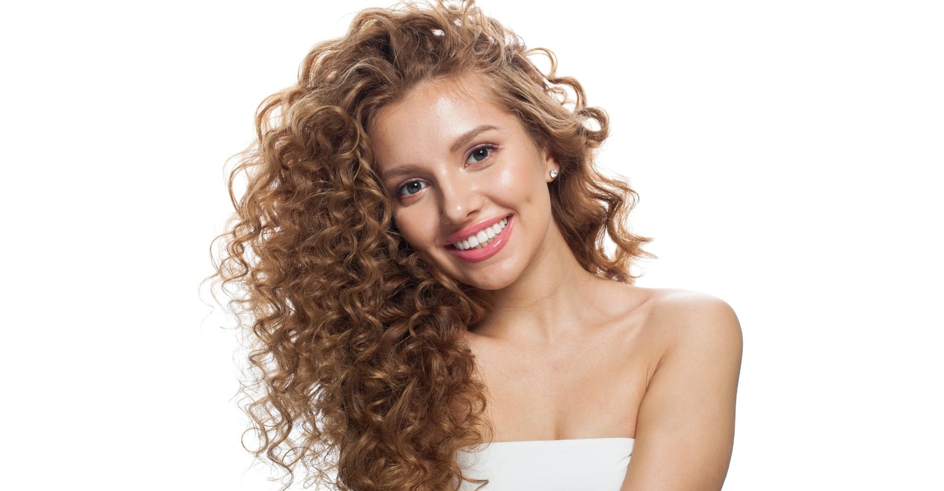 Mulher sorridente com cabelos longos castanho claro cacheados e brilhantes, mostrando fios com aspecto saudável e luminoso após tratamento com gloss para o cabelo.