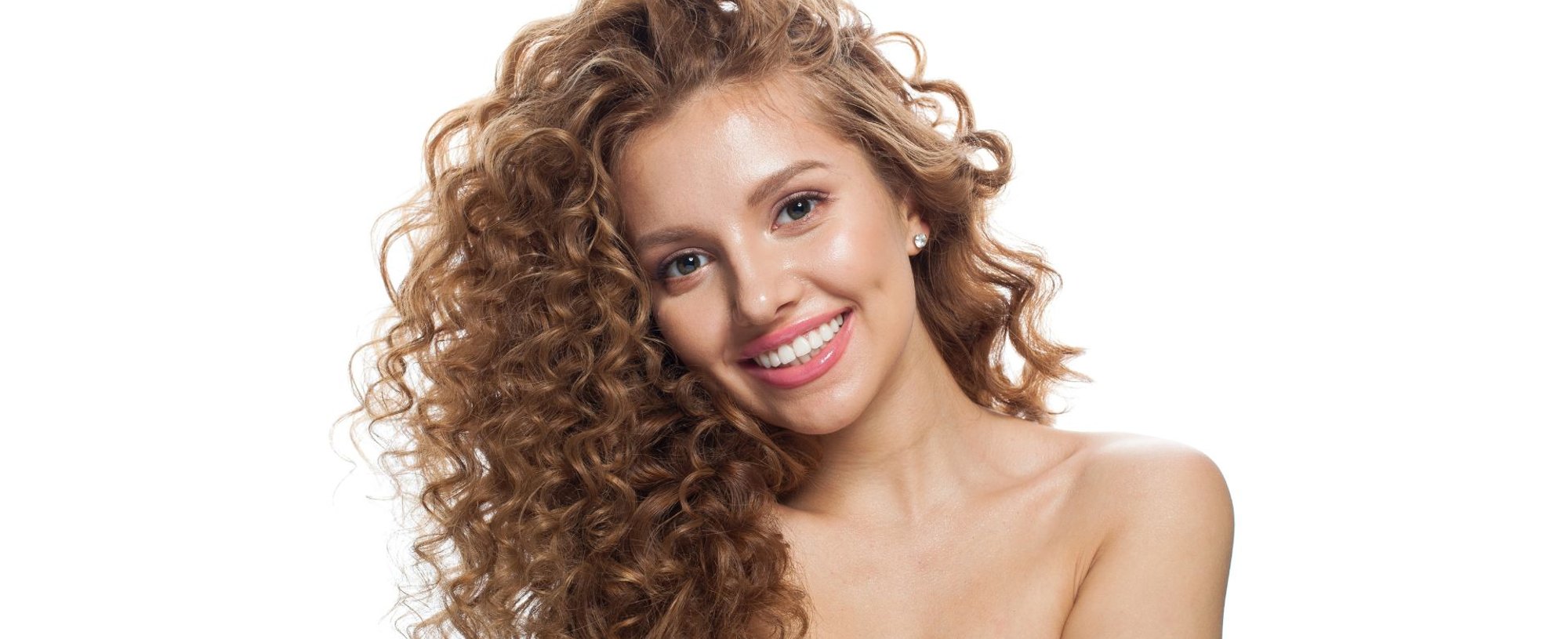Mulher sorridente com cabelos longos castanho claro cacheados e brilhantes, mostrando fios com aspecto saudável e luminoso após tratamento com gloss para o cabelo.
