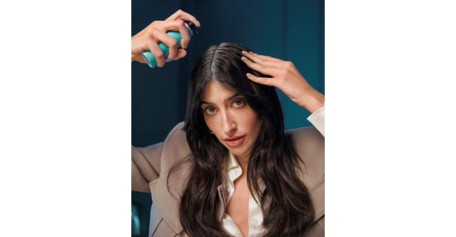 Mulher com cabelos escuros e raiz branca recebendo aplicação do spray Magic Retouch de L'Oréal Paris diretamente na raiz dos fios.