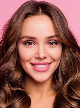 Mulher sorridente com cabelo brilhante após fazer banho de brilho no cabelo em fundo rosa.