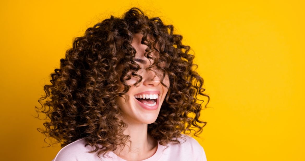 Mulher sorridente com cabelo cacheado em fundo amarelo.