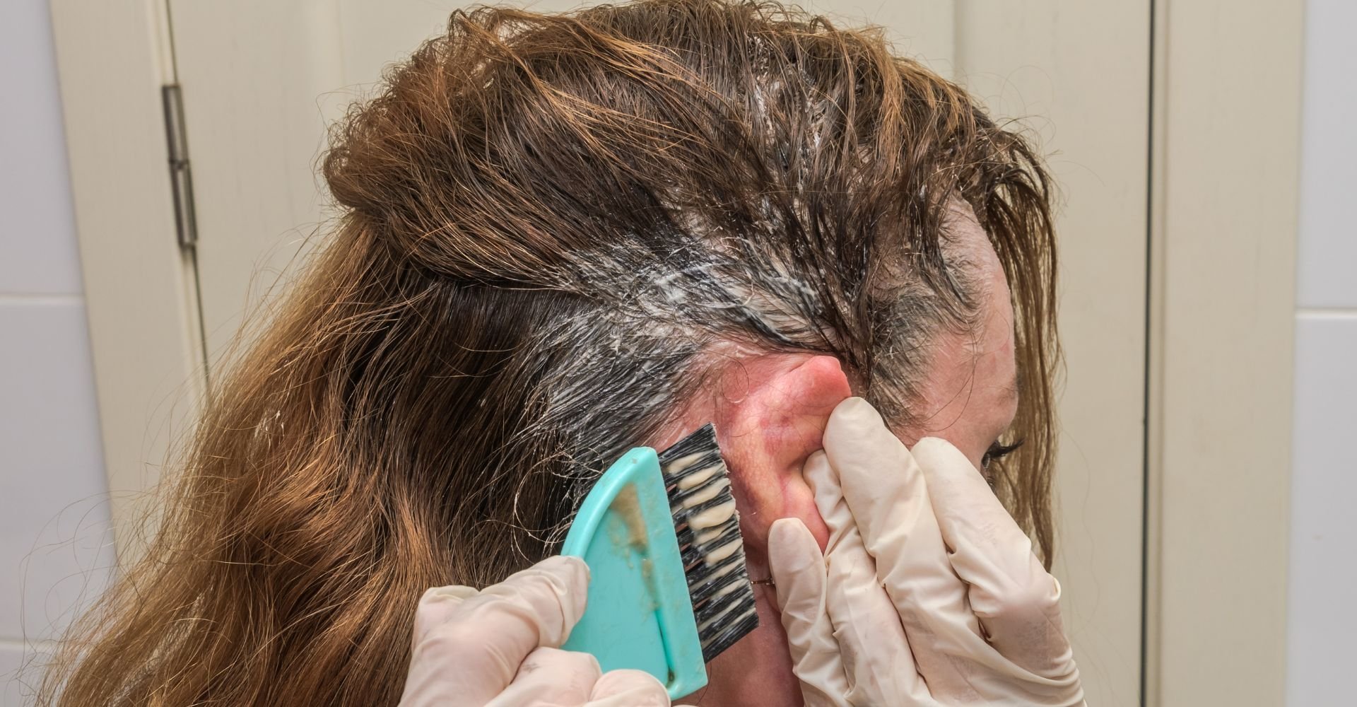 Mulher aplica tinta de cabelo nos fios em casa que pode ser retocada com spray para cabelo branco temporariamente.