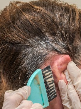 Mulher aplica tinta de cabelo nos fios em casa que pode ser retocada com spray para cabelo branco temporariamente.