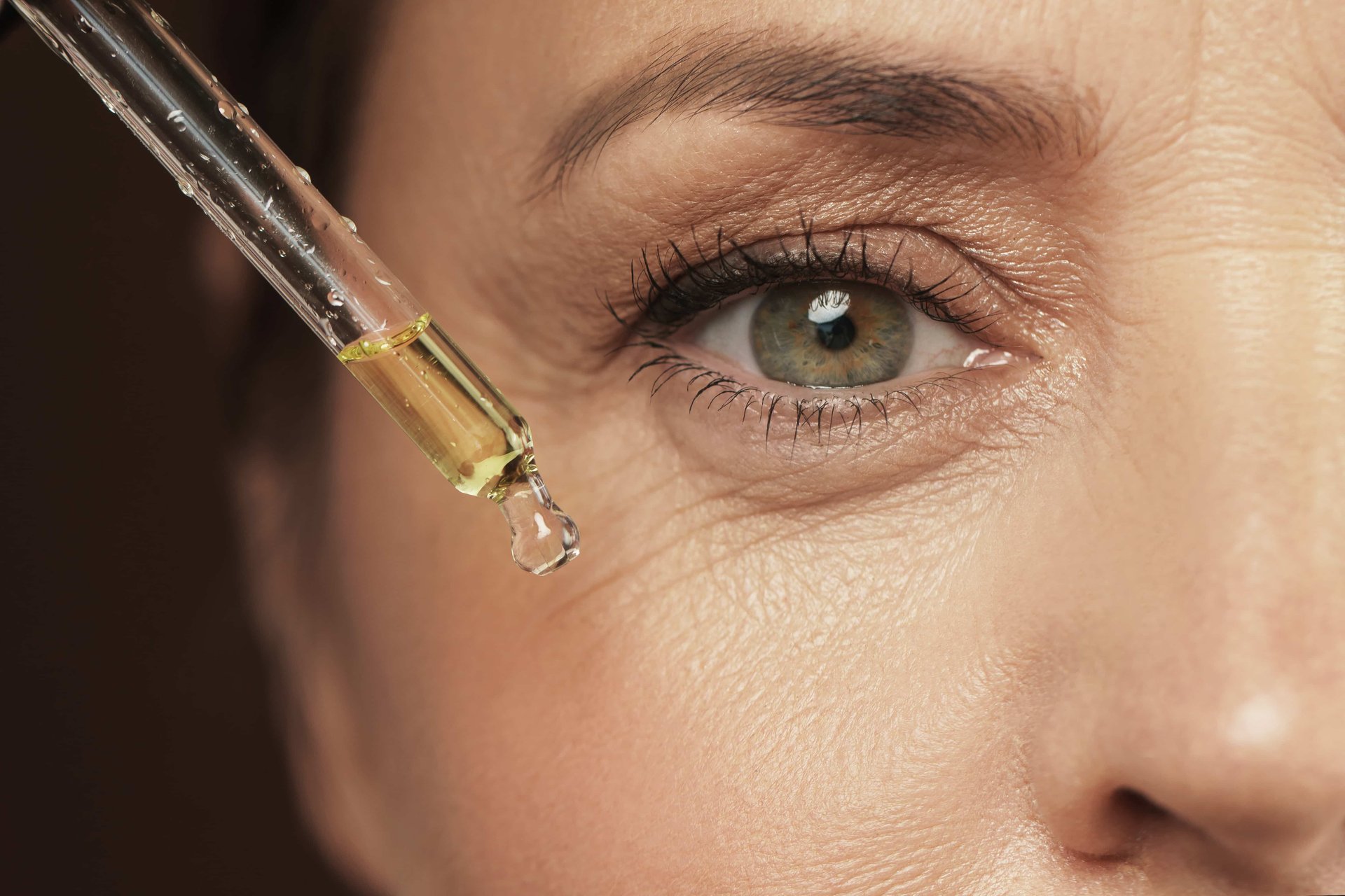 Mulher madura com rugas e pés de galinha aplica um sérum facial de bakuchiol na pele do rosto.