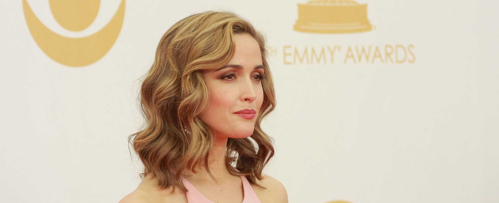 Atriz Rose Byrne com cabelos loiros e ondulados posando para foto