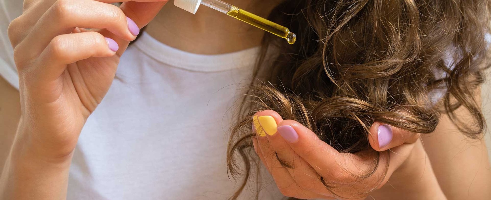 Modelo com cabelo cacheado castanho passando produto em seu cabelo