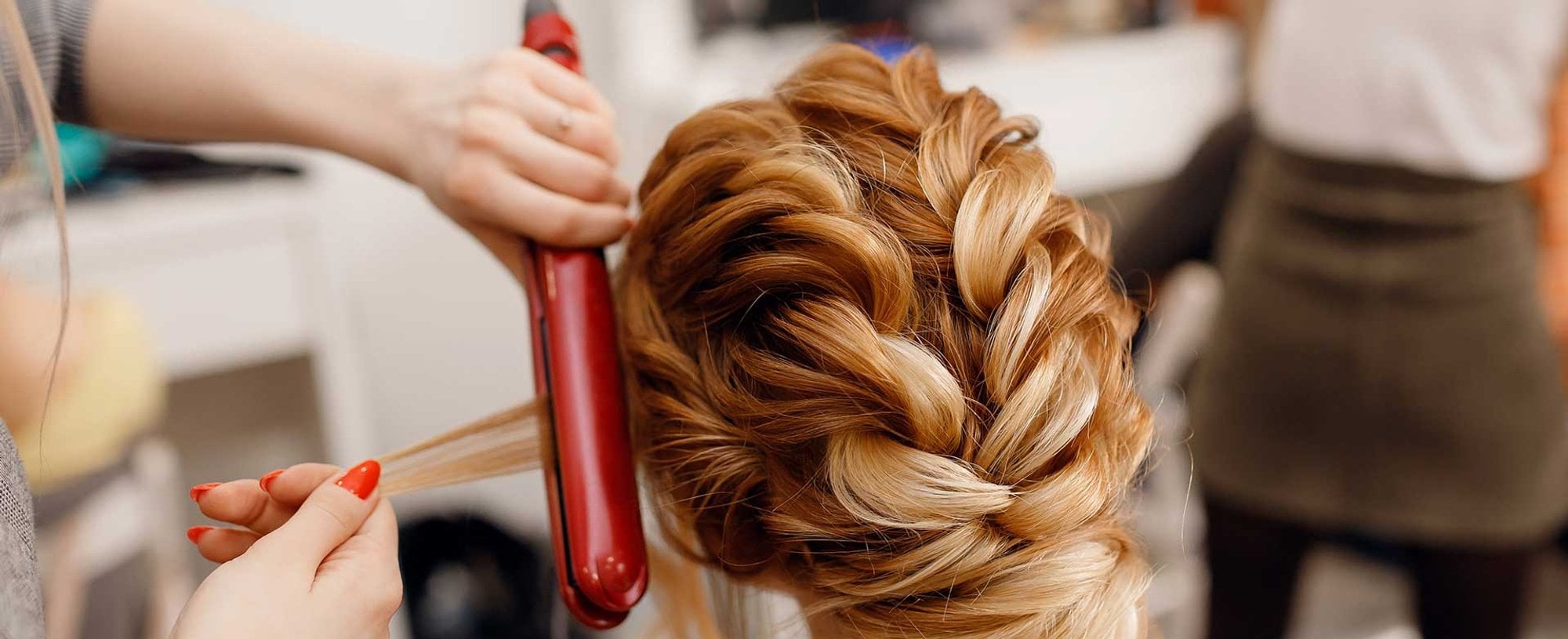 Profissional passando chapinha em um cabelo loiro