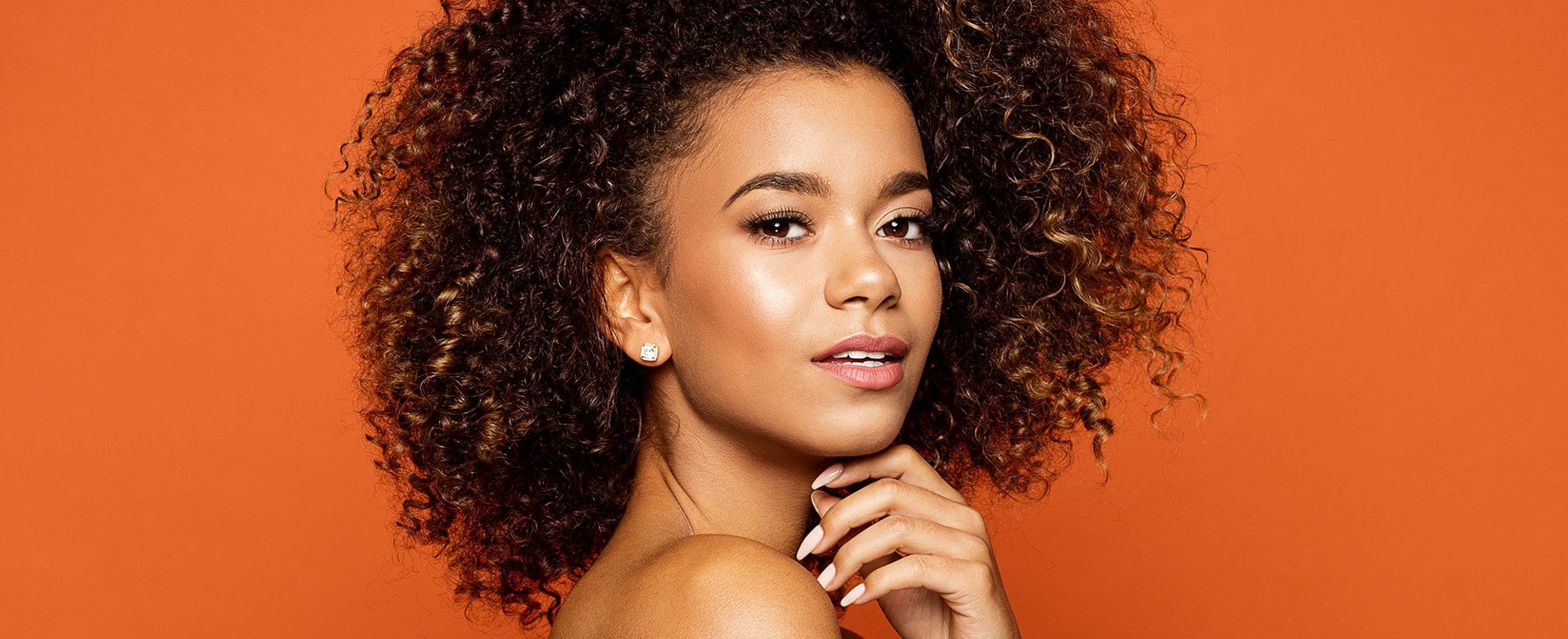 Modelo morena com cabelo cacheado volumoso com luzes nas pontas