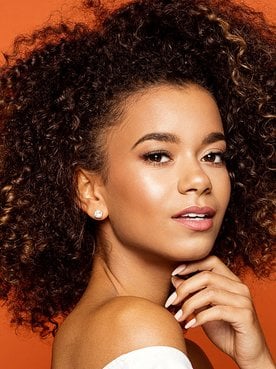 Modelo morena com cabelo cacheado volumoso com luzes nas pontas