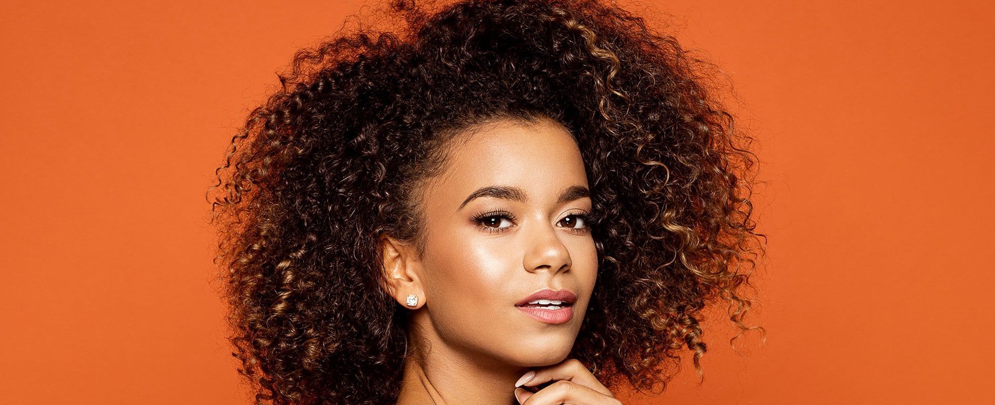 Modelo morena com cabelo cacheado volumoso com luzes nas pontas
