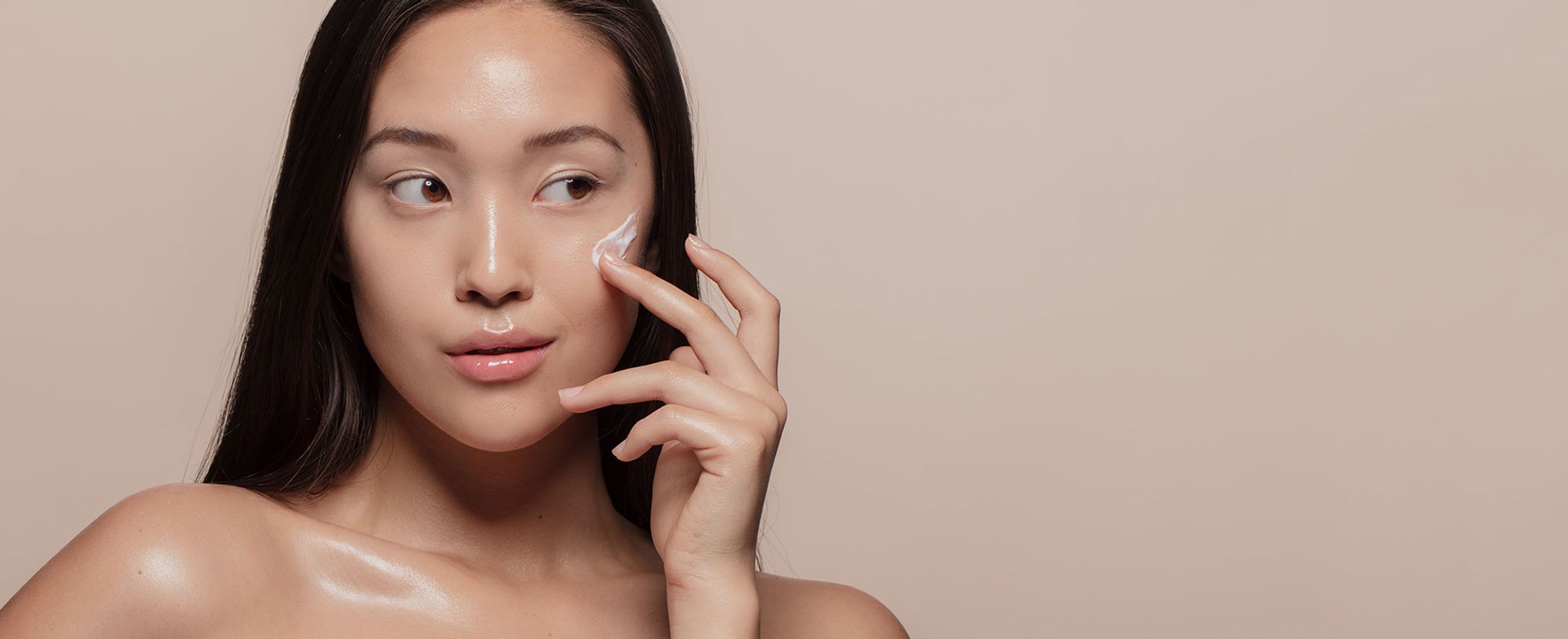 Modelo asiatica passando produto com textura de creme cor branca no rosto
