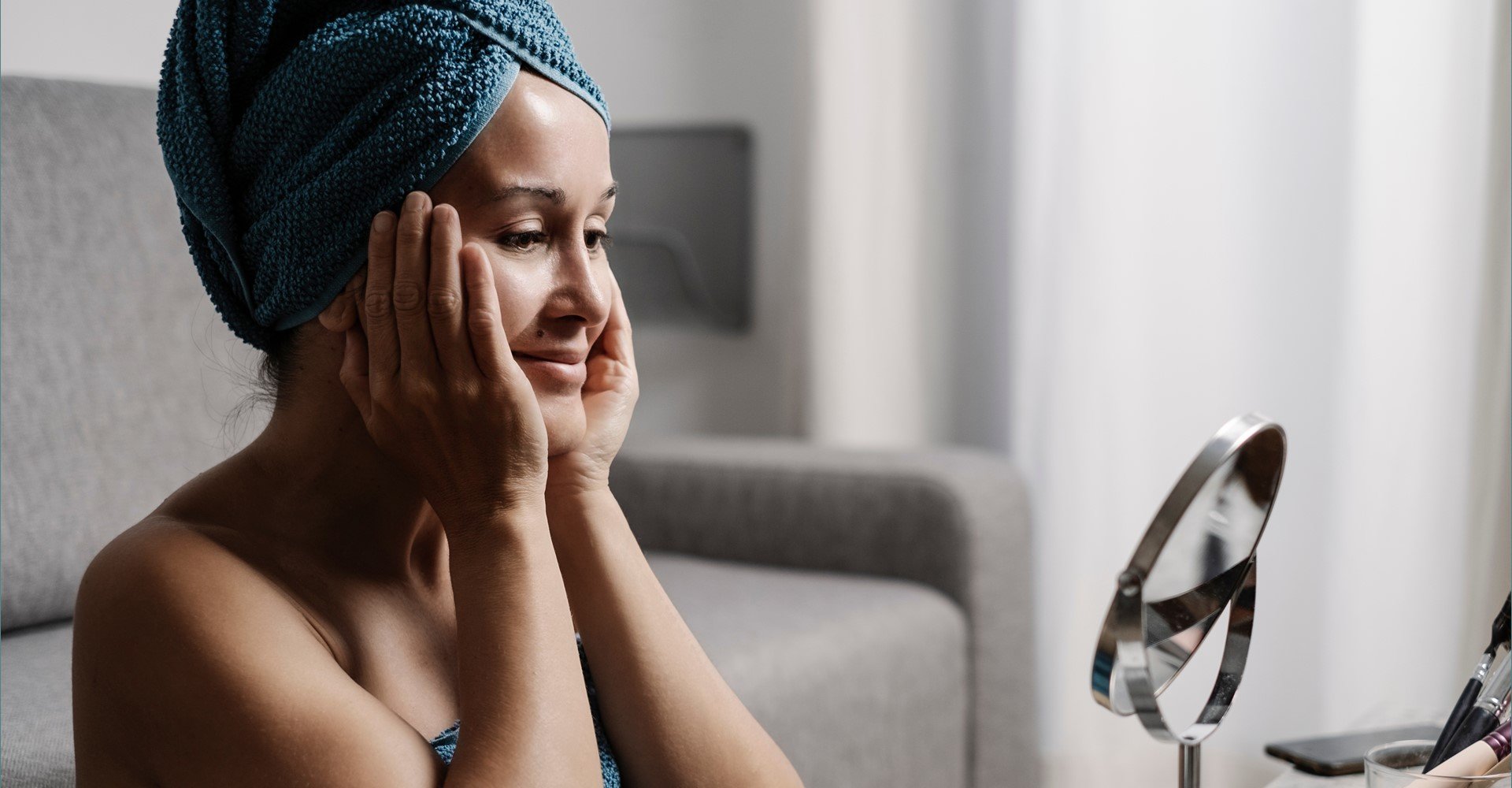 Modelo branca se olhando no espelho com as mãos no rosto e sorrindo