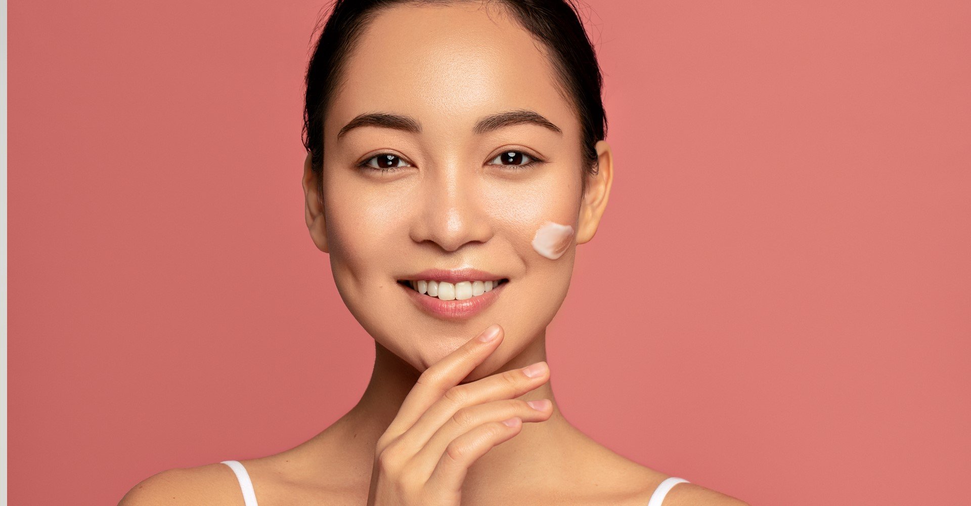 Modelo asiática sorrindo com creme no rosto