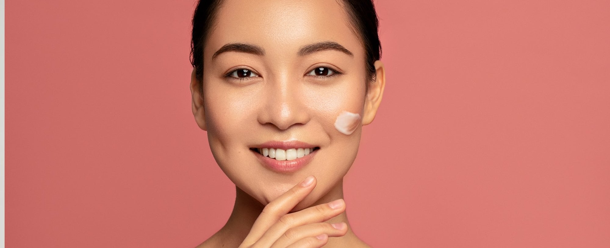 Modelo asiática sorrindo com creme no rosto
