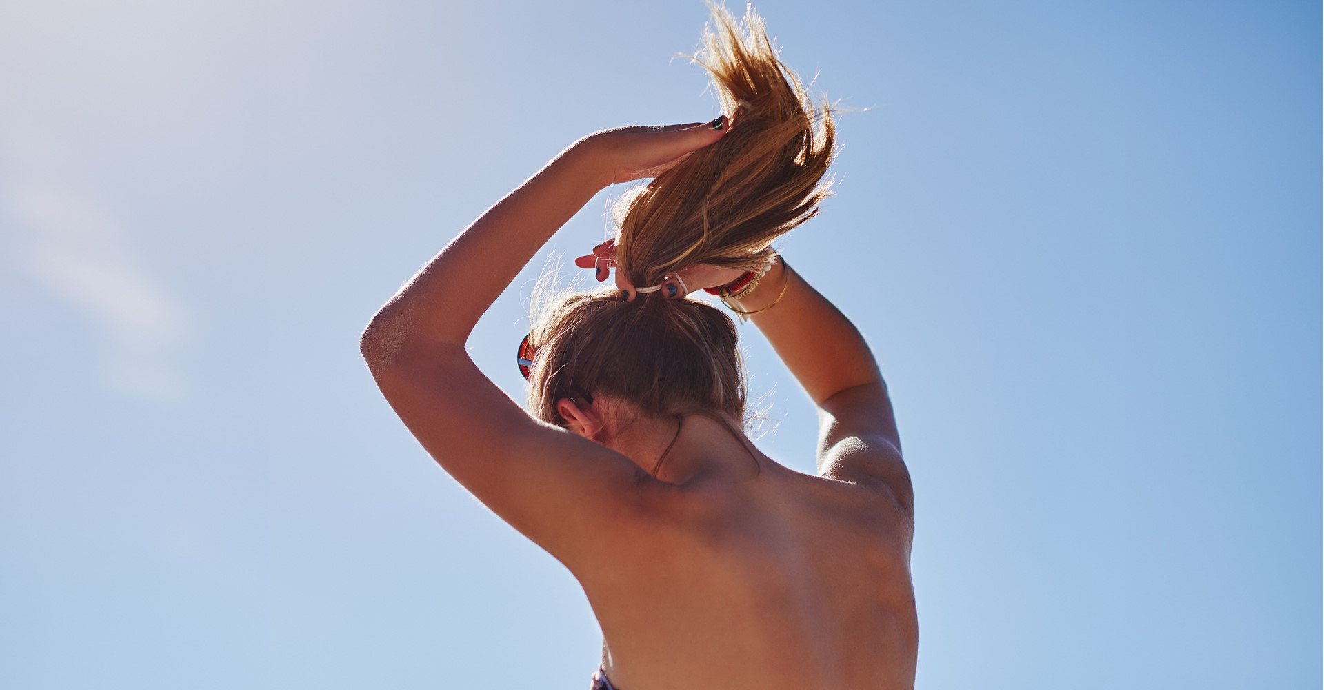 Modelo branca de costas amarrando o cabelo