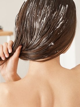 Modelo branca de costas passando creme no cabelo