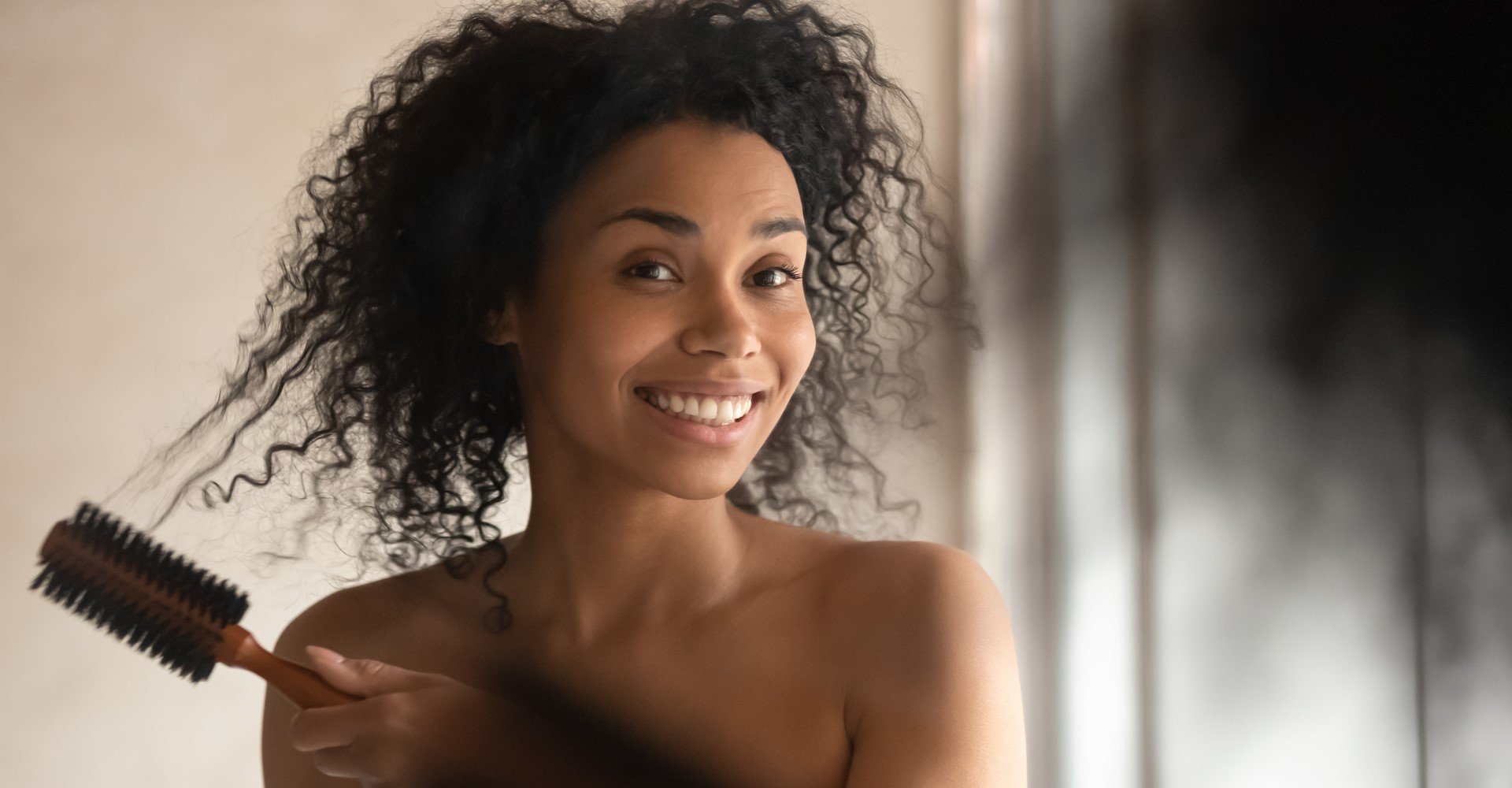 Modelo negra se olhando no espelho com cabelo cacheado