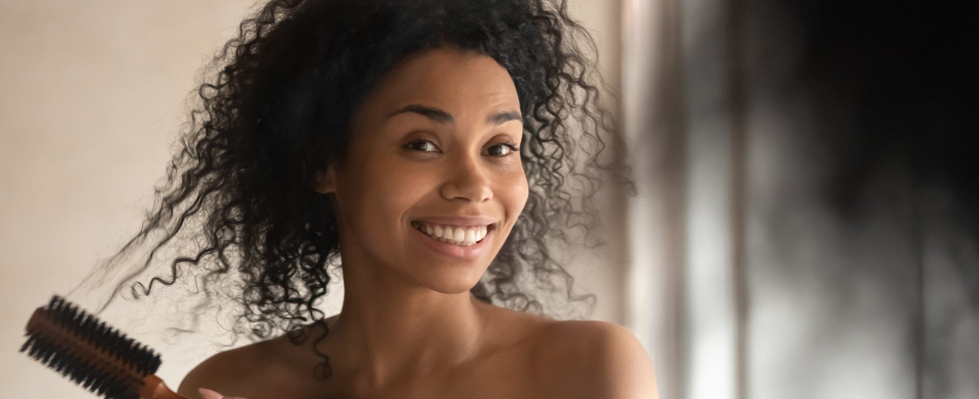 Modelo negra se olhando no espelho com cabelo cacheado