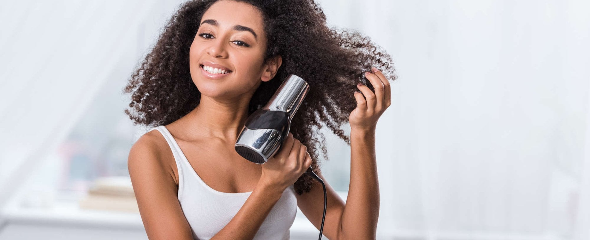 Modelo negra secando seus cabelos cacheados com secador