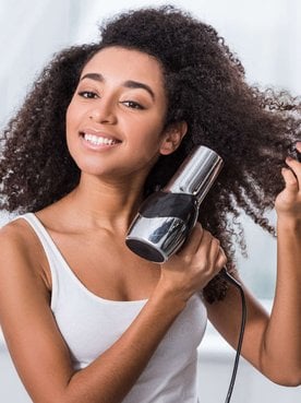 Modelo negra secando seus cabelos cacheados com secador
