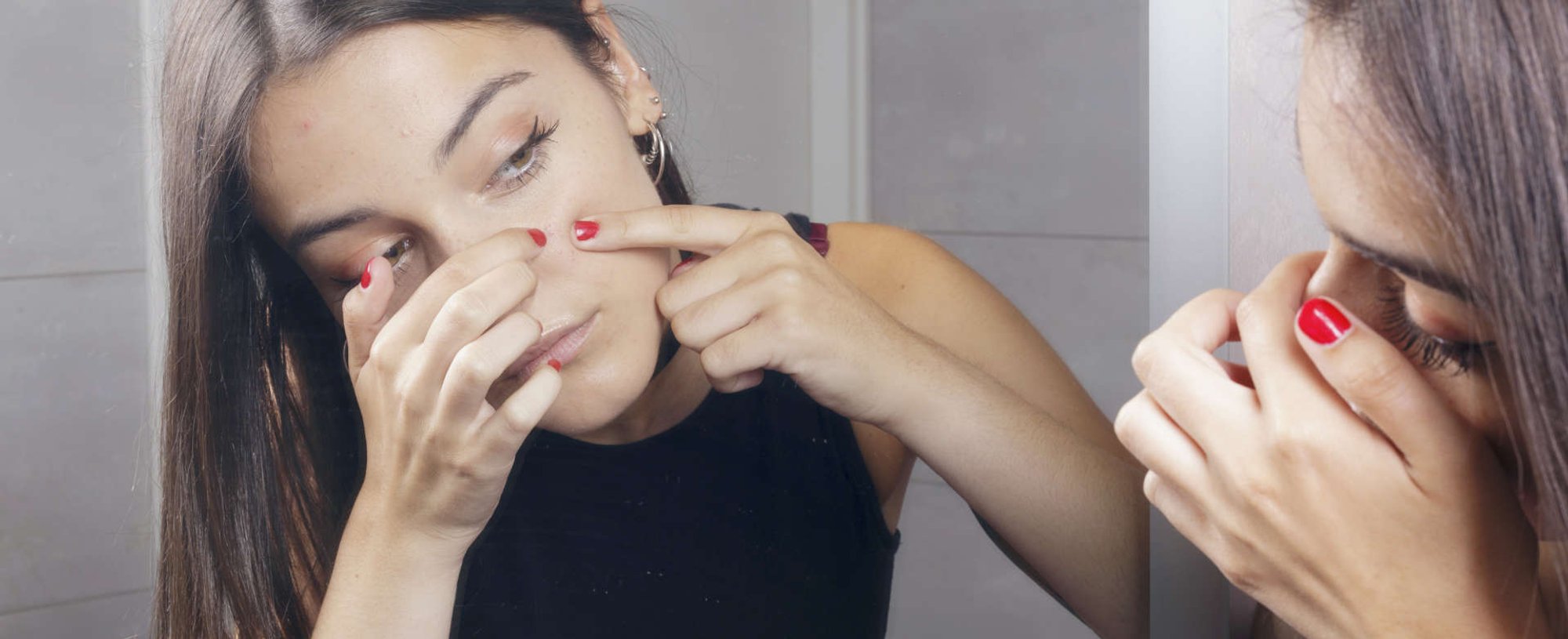 Modelo branca se olhando no espelho apertando acne