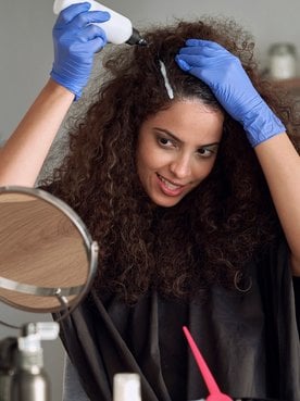 Modelo se olhando no espelho passando tinta no cabelo
