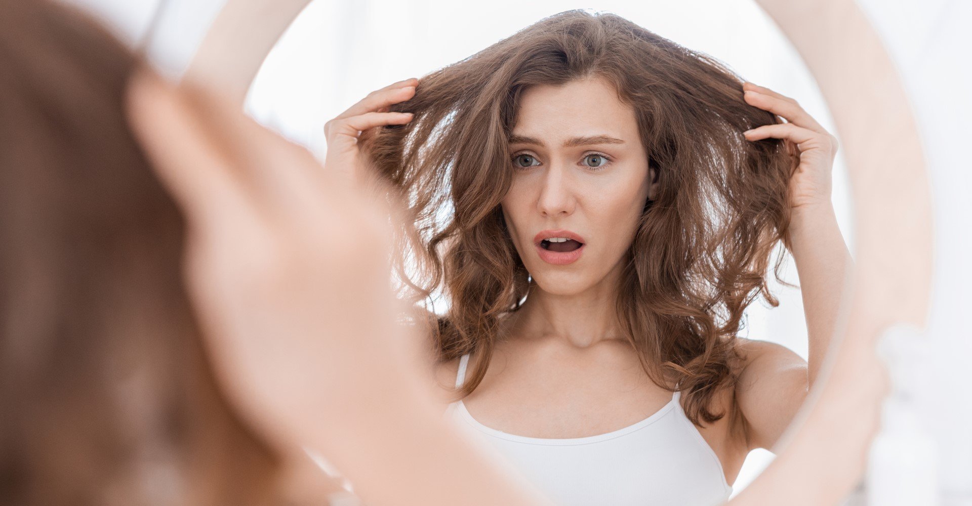 Modelo branca se olhando no espelho com expressão de espanto