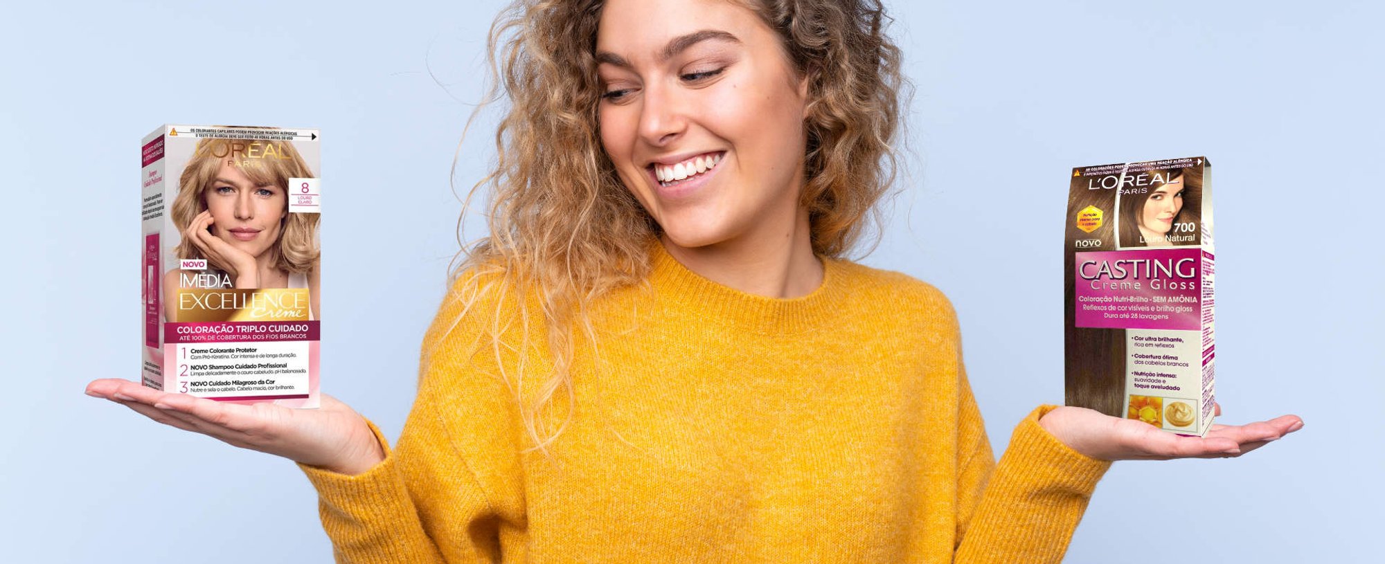 Modelo branca com cabelo loiro e cacheado segurando duas tintas da L'Oréal